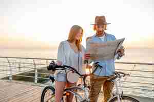 Kostenloses Foto attraktives glückliches paar, das im sommer auf fahrrädern, mann und frau mit blondem haar boho-hipster-art-mode reist, die spaß zusammen haben und in kartenbesichtigung schauen