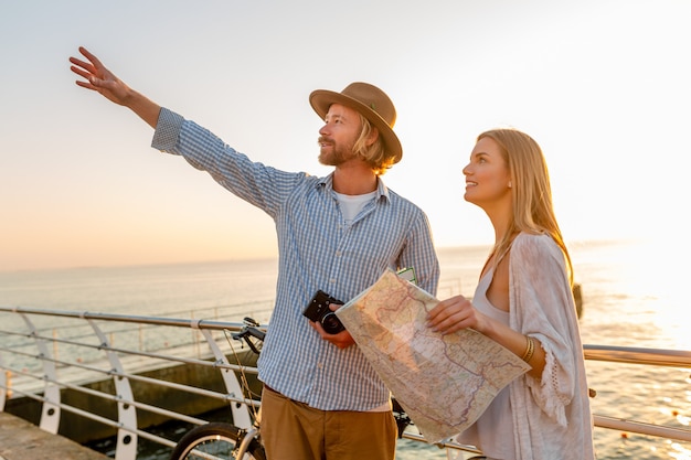 Attraktives glückliches Paar, das im Sommer auf Fahrrädern, Mann und Frau mit blondem Haar im Boho-Hipster-Stil unterwegs ist und Spaß zusammen hat