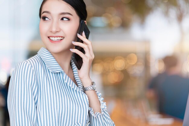 Attraktives, intelligentes, schönes asiatisches, gut gekleidetes Kommunikations-Smartphone mit fröhlichem und selbstbewusstem, unscharfem Hintergrund im öffentlichen Raum