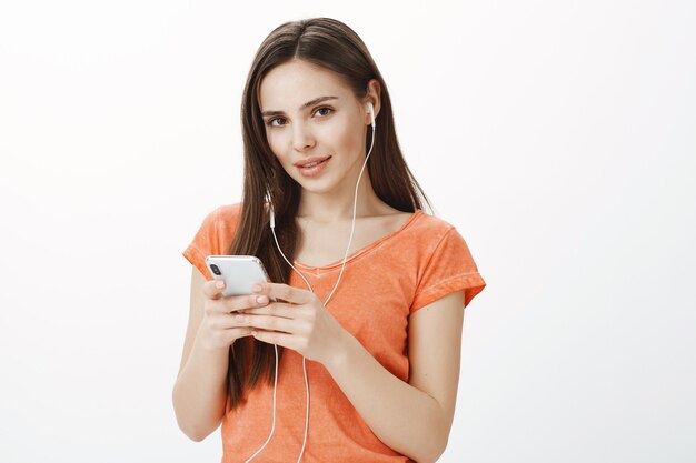 Attraktives junges brünettes Mädchen, das Musik in den Kopfhörern hört und Handy hält