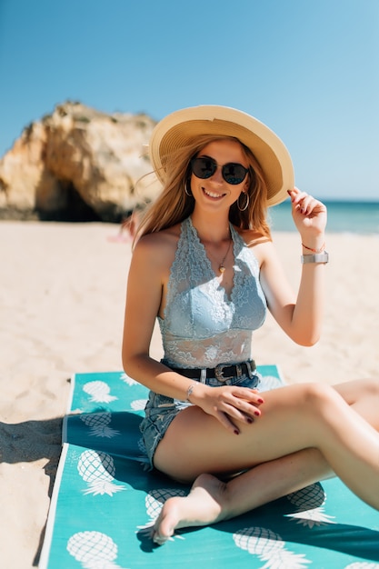 Attraktives Mädchen in Sonnenbrille und Hut liegt auf warmem Sand