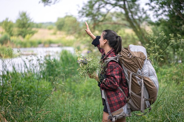 Attraktives Mädchen mit einem großen Reiserucksack und einem Strauß Wildblumen.