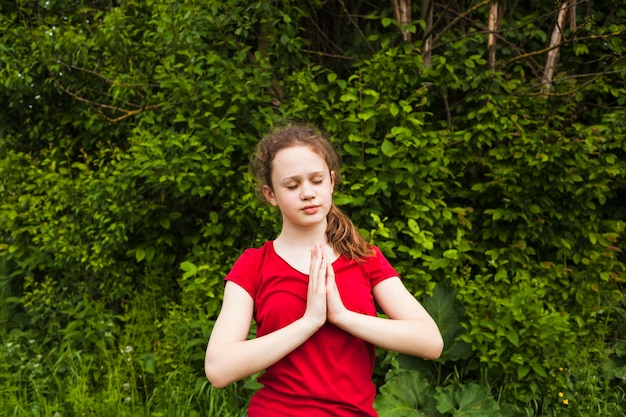 Attraktives Mädchenkind, das mit geschlossenen Augen in der Natur betet