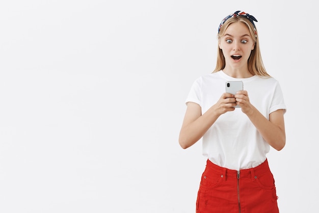 Attraktives modernes Mädchen, das Handy benutzt und überrascht schaut