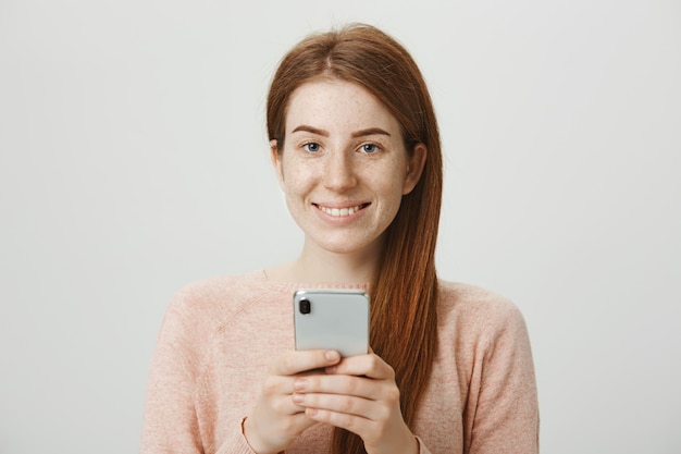 Attraktives rothaariges lächelndes Mädchen, das Handy, Nachrichten verwendet