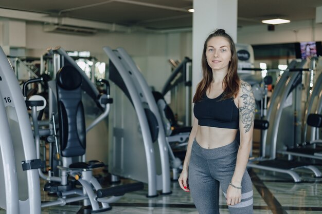 Attraktives sportliches Mädchen steht an der Wand der Simulatoren im Fitnessstudio. gesunder Lebensstil.