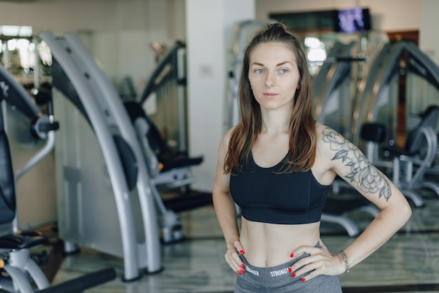 Kostenloses Foto attraktives sportliches mädchen steht auf dem hintergrund der simulatoren im fitnessstudio. gesunder lebensstil.