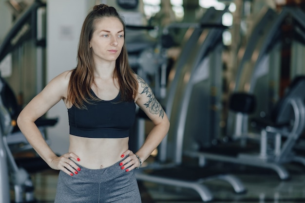 Attraktives sportliches Mädchen steht auf dem Hintergrund der Simulatoren im Fitnessstudio. gesunder Lebensstil.