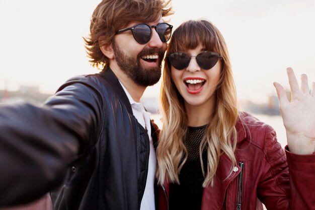 Attraktives stilvolles Paar in der Liebe, die im Freien aufwirft, umarmt und auf Kai geht. Weiche Abendfarben. Modischer Look. Trendige Sonnenbrille. Mann und Frau peinlich.