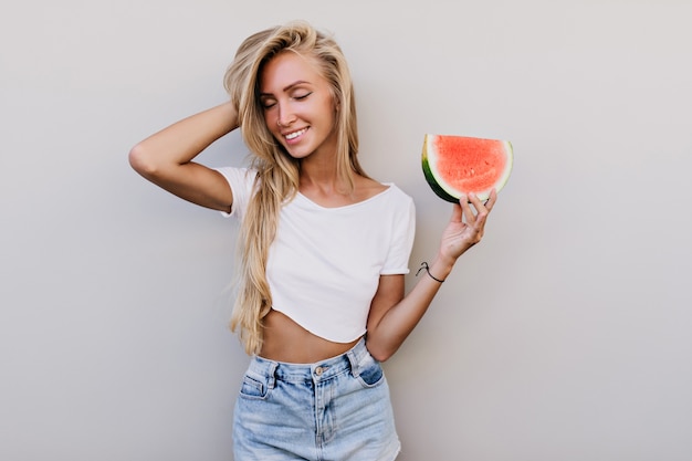 Attraktives weißes weibliches Modell in der Wassermelone, die Tank-Top hält.