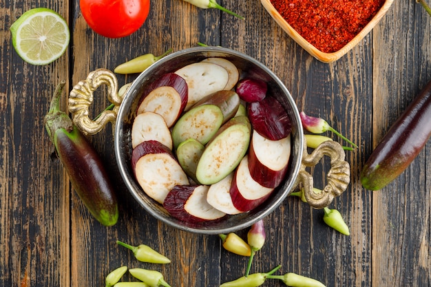 Auberginen mit Gewürzen, Paprika, Tomaten, Limette in einer Pfanne auf Holz, flach gelegt.