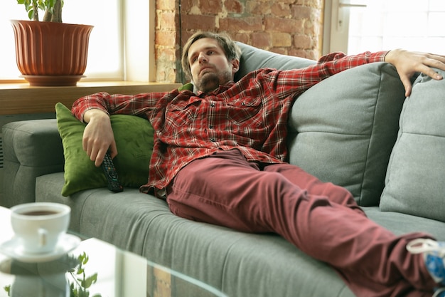 Kostenloses Foto auf dem sofa liegend fernsehen. kaukasischer mann, der während der quarantäne zu hause bleibt