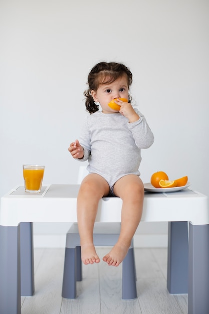 Auf dem Tisch sitzen Baby, das Orange isst