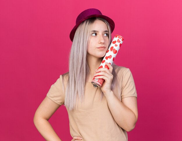 Auf der Suche nach Seite junges schönes Mädchen mit Partyhut mit Konfettikanone isoliert auf rosa Wand