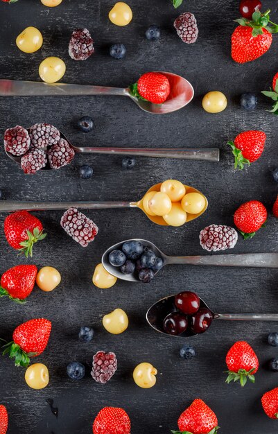 Auf einem dunklen Tisch lagen Kirschen in Löffeln mit Erdbeeren, Blaubeeren, Maulbeeren flach