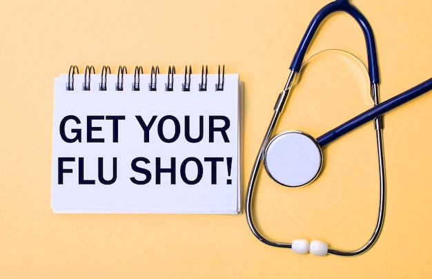 Auf einer beigen oberfläche befinden sich ein stethoskop und ein weißer notizblock mit der aufschrift get your flu shot