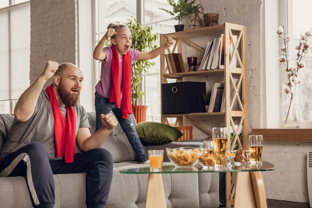 Aufgeregt, glückliche Tochter und Vater, die auf der Couch zu Hause Fußball, Fußball, Basketball, Tennis und Hockey schauen.