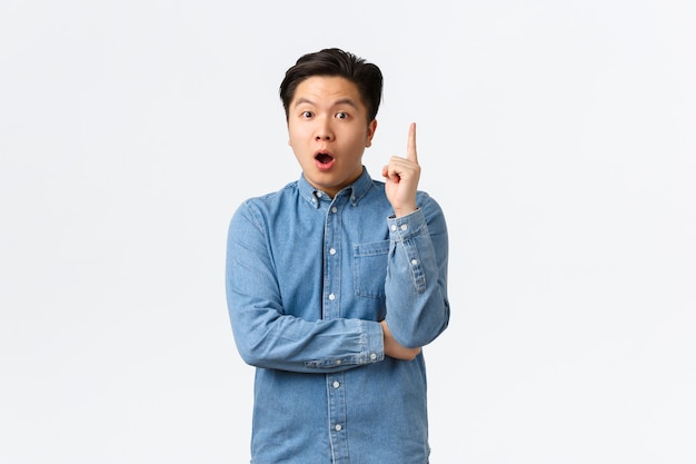Aufgeregt intelligenter und kreativer asiatischer Mann im Hemd mit Idee. Kerl macht einen Vorschlag, denkt sich einen großartigen Plan aus, hebt den Zeigefinger in der Heureka-Geste, sagt seine Meinung, steht auf weißem Hintergrund.