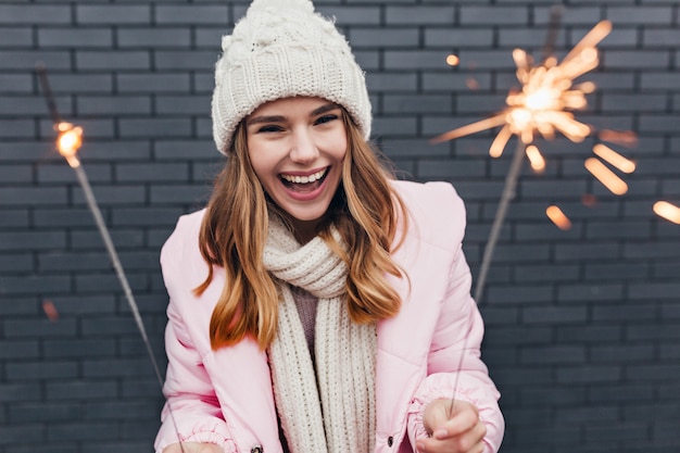 Aufgeregte blonde Frau in romantischer Kleidung, die neues Jahr feiert. Foto im Freien des fröhlichen Mädchens in der Strickmütze, die in Weihnachten kühlt.