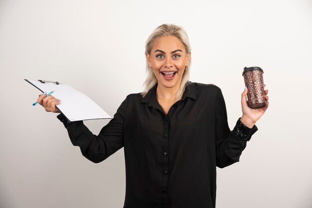 Aufgeregte Frau, die eine Tasse mit Klemmbrett auf weißem Hintergrund hält. Hochwertiges Foto