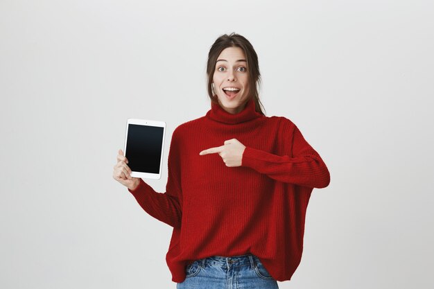 Aufgeregte Frau, die Finger auf digitalen Tablettbildschirm zeigt