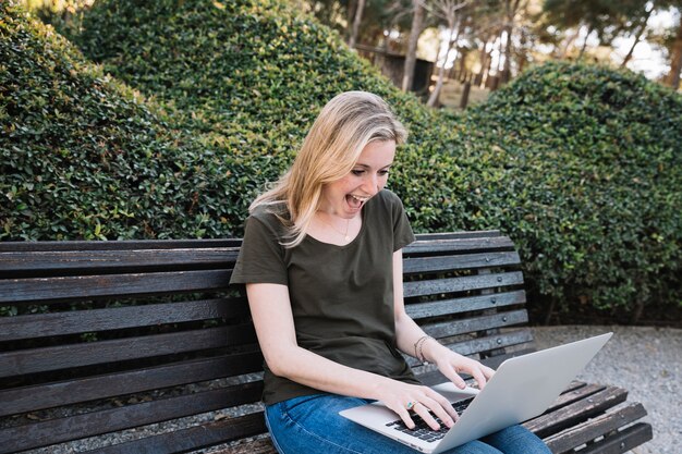 Aufgeregte Frau, die Laptop im Park verwendet