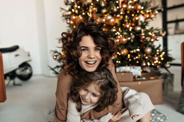 Aufgeregte glückliche Frau mit der kleinen Tochter, die lacht und Spaß hat, während sie Weihnachten feiert