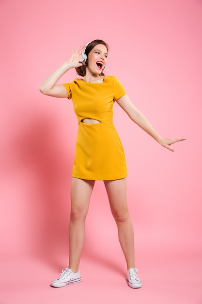 Aufgeregte glückliche junge Dame im gelben Kleid tanzen