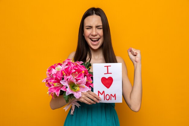 Aufgeregte junge Frau, die den Muttertag feiert und Grußkarte und Blumenstrauß hält