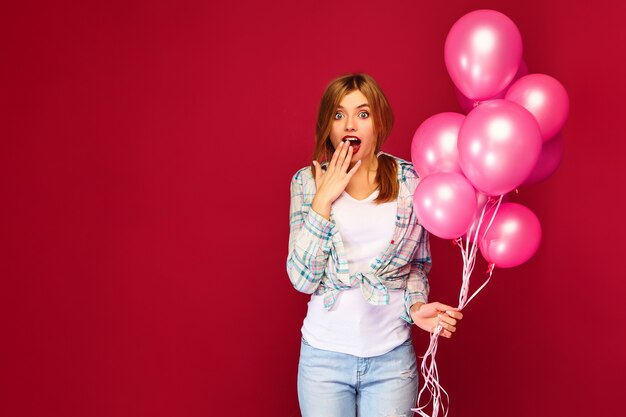 Aufgeregte junge Frau, die mit rosa Luftballons aufwirft