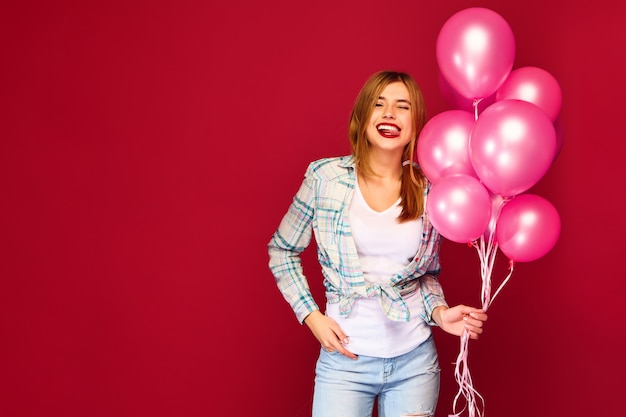 Aufgeregte junge Frau, die mit rosa Luftballons aufwirft