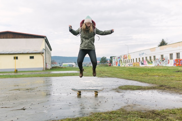 Aufgeregte junge Frau, die über Skateboard springt