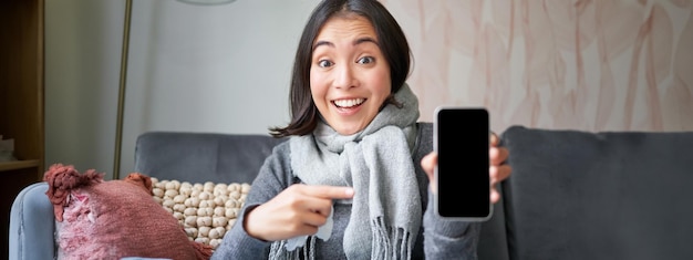 Aufgeregte junge Frau zeigt mit dem Finger auf das Smartphone und zeigt eine Online-Arztanwendung oder einen Hausarzt an