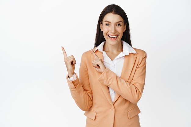 Aufgeregte Verkäuferin, die lächelnd mit dem Finger auf die obere linke Ecke zeigt, während sie die Produktwerbung des Unternehmens demonstriert, die über weißem Hintergrund steht