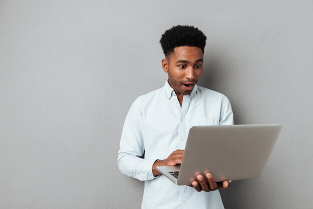 Aufgeregter afroamerikanischer Mann, der Laptop-Computerbildschirm betrachtet