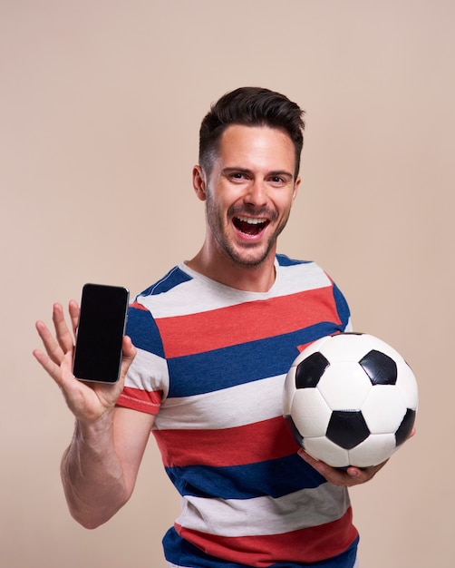 Aufgeregter Fan, der Fußball hält und Handy zeigt