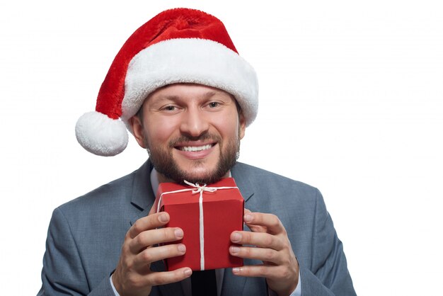 aufgeregter fröhlicher Geschäftsmann, der lächelnd eine kleine Weihnachtsgeschenkbox an sein Gesicht hält