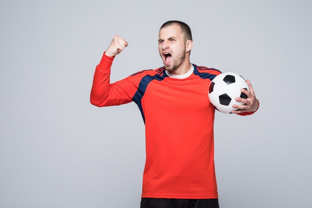 Aufgeregter Fußballspieler im roten T-Shirt, der ein Fußball-Siegeskonzept lokalisiert auf Weiß hält