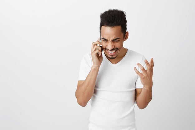 Aufgeregter glücklicher afroamerikanischer Mann, der am Telefon spricht und fröhlich lächelt