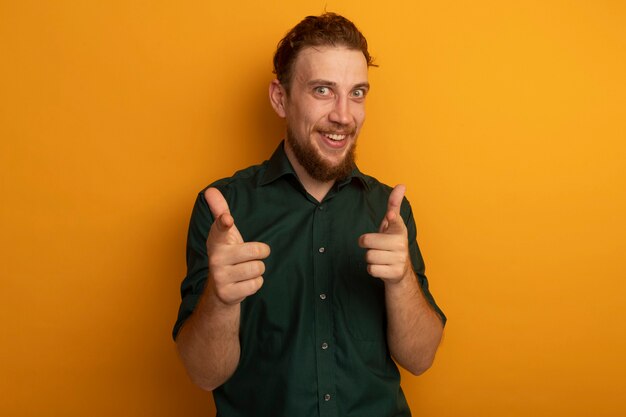 Aufgeregter hübscher blonder Mann zeigt mit zwei Händen auf Orange auf Kamera