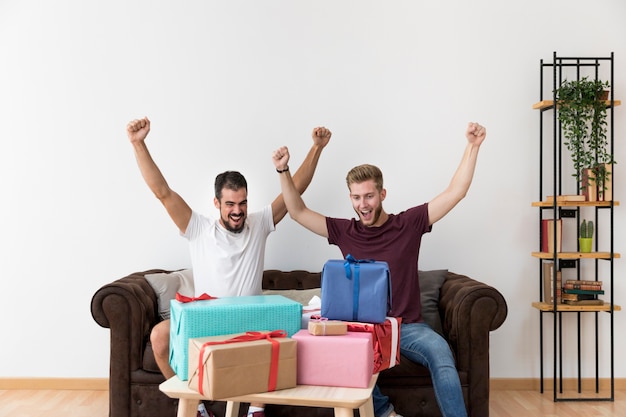 Aufgeregter junger Mann, der auf dem Sofa betrachtet bunte Geschenkboxen sitzt