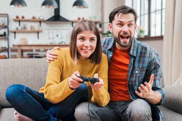 Aufgeregter junger Mann, der mit ihrer Frau spielt das Videospiel sitzt