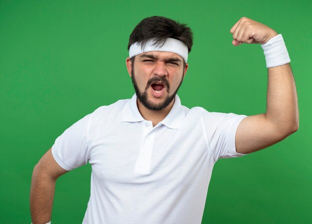 Aufgeregter junger sportlicher Mann, der Stirnband und Armband trägt und starke Geste zeigt