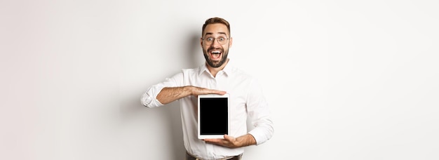 Aufgeregter mann, der einen digitalen tablet-bildschirm zeigt, der erstaunt über weißem hintergrund steht