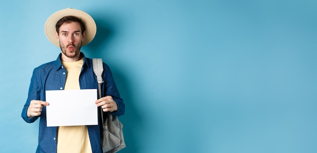 Kostenloses Foto aufgeregter tourist mit strohhut, der ein leeres blatt papier hält und amüsiert aussieht, wenn er auf sommerreise geht