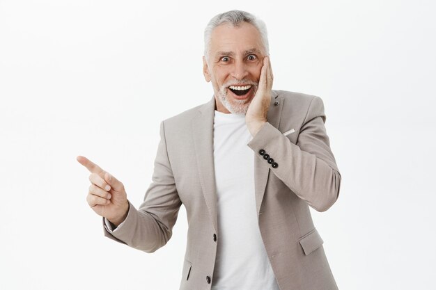 Aufgeregter und überraschter älterer Mann, der mit dem Finger nach links zeigt und erstaunt lächelt