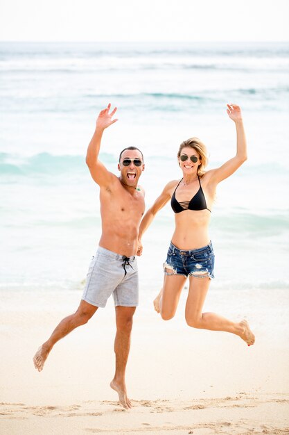 Aufgeregtes junges Paar springt am Strand