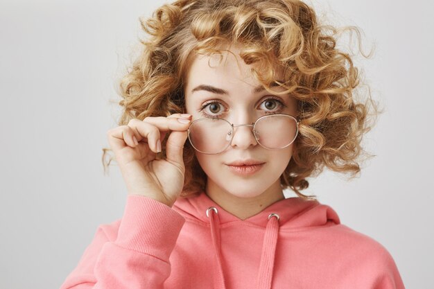 Aufgeregtes lockiges Mädchen, das an Brille interessiert aussieht