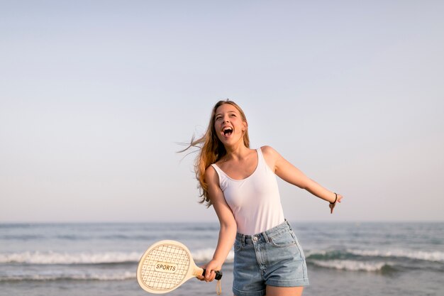 Aufgeregtes Mädchen, das vor der Küste spielt Tennis steht