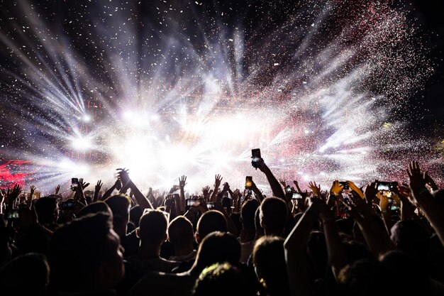 Aufgeregtes Publikum, das Konfetti-Feuerwerk beobachtet und sich nachts auf dem Musikfestival amüsiert Kopieren Sie Platz